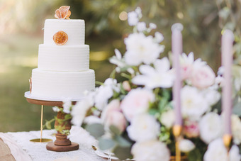 Dreistöckige weiße Hochzeitstorte mit getrockneten Orangenscheiben, daneben Blumenarrangement in Pastelltönen